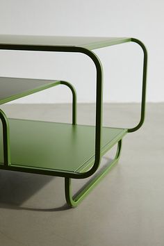 a green table sitting on top of a cement floor next to a white wall with an open shelf underneath it