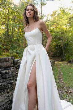 a woman in a white dress standing next to a stone wall with her legs high