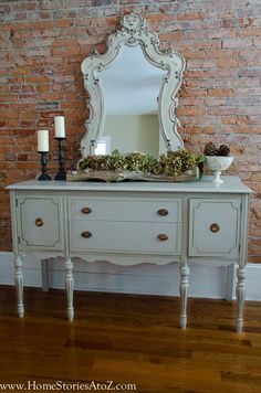 a white dresser sitting next to a brick wall with a large mirror on top of it