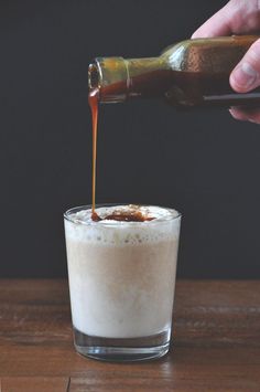 someone pouring something into a glass on top of a wooden table