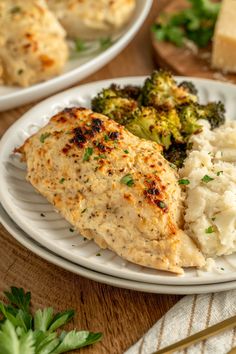 two white plates topped with chicken, broccoli and mashed potatoes on a wooden table