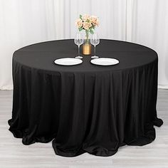 a round table with two wine glasses on it and a vase full of flowers in the middle