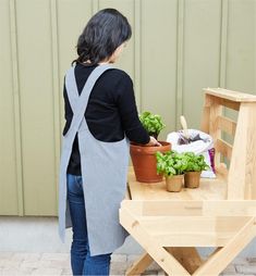 a woman standing next to a wooden table with potted plants on top of it