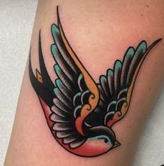 a colorful bird tattoo on the leg with black and orange wings flying in the air