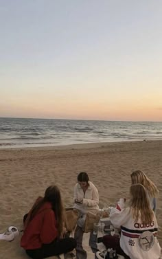 four people sitting on the beach at sunset