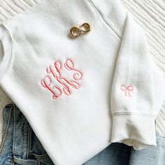 "*Model shown wearing a white medium sweatshirt with Coral Pink thread, font#3* Our embroidered monogram crewneck just got cuter! Customize this classic crew with a personalized monogram design plus a super sweet and trendy mini bow embroidered on the sleeve! These are unisex sizing.  8-ounce, 50/50 cotton/poly Double-needle stitching at waistband and cuffs 1x1 rib knit collar, cuffs and waistband with spandex **NOT PROVIDING ALL OF THE REQUIRED INFORMATION FOR PERSONALIZATION WILL DELAY YOUR ORDER.** When checking out, put this information in the \"NOTES TO SELLER\" section: 1. Monogram*, Full Name or Initial . Please note, we will not rearrange letters, will be embroidered as provided (Fonts 5, 14 and 18 are initial format fonts - all letters are the same size) 2. Font Option  3. Monogra Sweatshirt With Initials, White Crew Neck Sweatshirt With Embroidered Logo, White Embroidered Logo Crew Neck Sweatshirt, White Classic Sweatshirt For Spring, Classic White Sweatshirt For Spring, Classic White Spring Sweatshirt, Machine Embroidery Shirts, Preppy Long Sleeve Cotton Sweatshirt, Classic White Letter Print Sweater