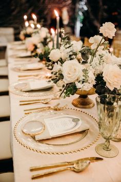 a long table is set with white flowers and gold place settings for an elegant dinner