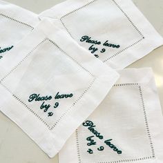 three embroidered napkins with words on them sitting next to each other in front of a white table