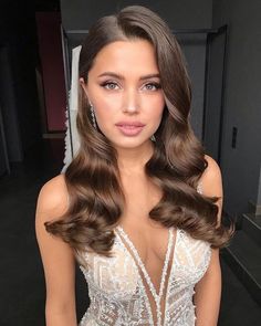 a woman with long brown hair wearing a white dress and posing for the camera in front of a mirror