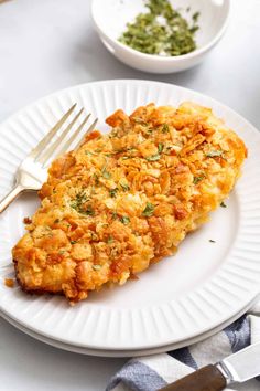 a white plate topped with an omelet next to a bowl of green herbs