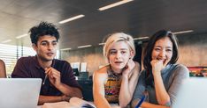 three people sitting at a table with laptops and papers in front of their faces