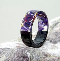 a wedding ring with purple and gold inlays sitting on top of a rock