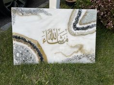 a white marble with gold and black designs on it in the grass next to some flowers