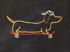 a dog on a skateboard embroidered onto a black t - shirt with yellow thread