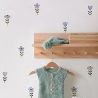 a baby's sweater hanging on a coat rack next to a wall with purple flowers