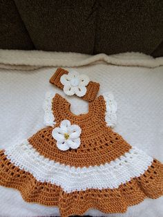 an orange and white crocheted baby dress with flowers on the bottom is laying on a pillow