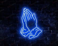 a neon blue praying hands on a brick wall