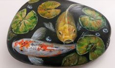 a hand holding a painted rock with fish and lily pads