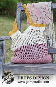 a crocheted bag sitting on top of a wooden bench next to a blanket