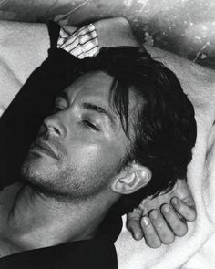 a black and white photo of a man laying in bed with his head on the pillow