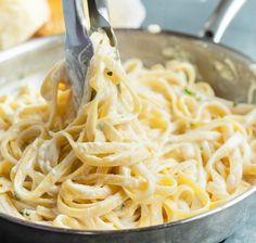 someone is using tongs to stir noodles in a pan