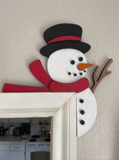 a snowman is hanging on the wall in front of a mirror with a red scarf and black hat