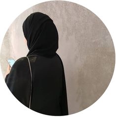 a woman in a black hoodie looking at her cell phone while standing against a wall