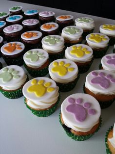 cupcakes with white frosting and colored paw prints are arranged on a table