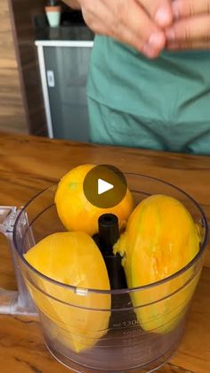 a glass bowl filled with lemons on top of a wooden table next to a person