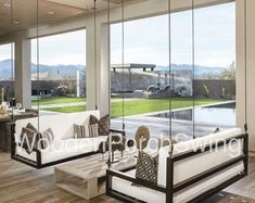 a living room filled with white furniture and large windows overlooking a swimming pool in the distance