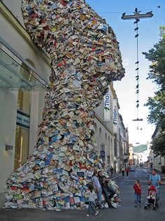 people are standing in front of a large sculpture made out of books on the street