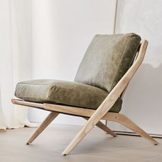 a wooden chair with a green cushion on it's back and legs in front of a window