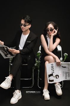 a man and woman sitting next to each other in front of a black background holding papers