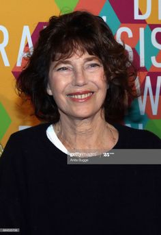 an older woman smiling at the camera in front of a colorful wall with words on it