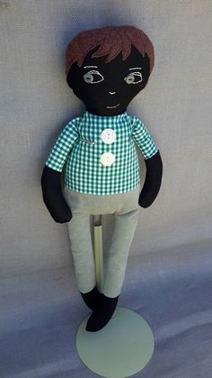 a black doll sitting on top of a green and white checkered cloth covered floor