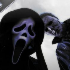 a man in a black jacket with a purple mask on his face next to another person