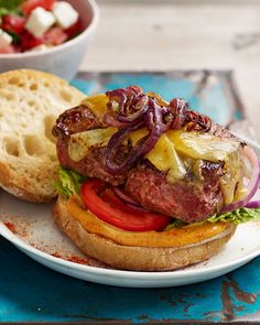 a hamburger with onions, tomato and lettuce is on a plate next to a bowl of salad