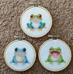 three cross - stitch frog pictures are displayed on the floor