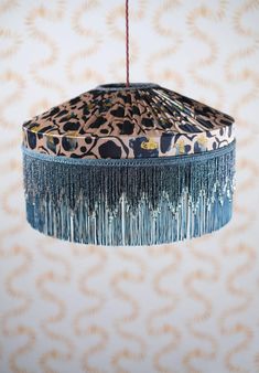 an animal print lamp shade hanging from a ceiling fixture with tassels on it