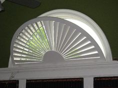 an open window with white shutters and blinds on the top shelf in front of a green wall