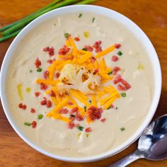 a white bowl filled with soup and cheese on top of a wooden table next to two spoons