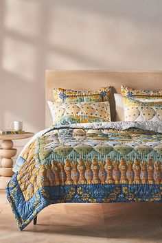 a bed with colorful quilts and pillows on top of it in a room next to a table