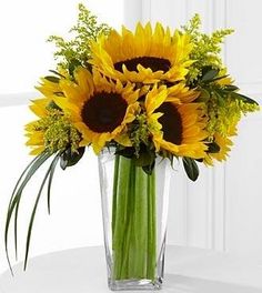 a vase filled with lots of yellow sunflowers on top of a white table