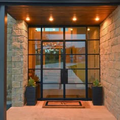 an entrance to a building with glass doors and lights on the outside wall, along with potted plants