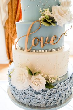 a three tiered cake with flowers and the word love on top