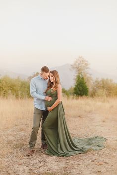 a pregnant couple standing in the middle of a field with their arms around each other