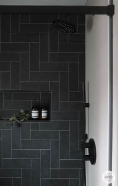 a black tiled bathroom with shelves and shower faucet in the corner on the wall