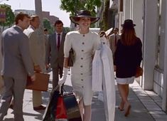 a woman in a white dress and hat walking down the street