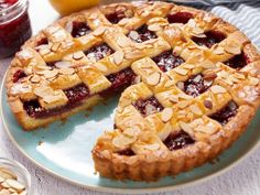 a pie on a plate with two slices cut out and some fruit in the background