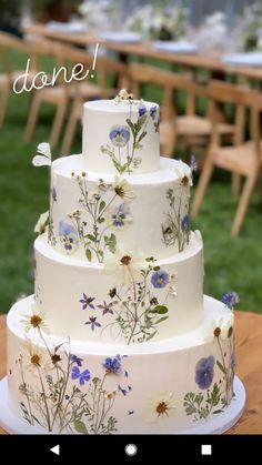 a three tiered wedding cake with blue and white flowers on the bottom, sitting on top of a wooden table